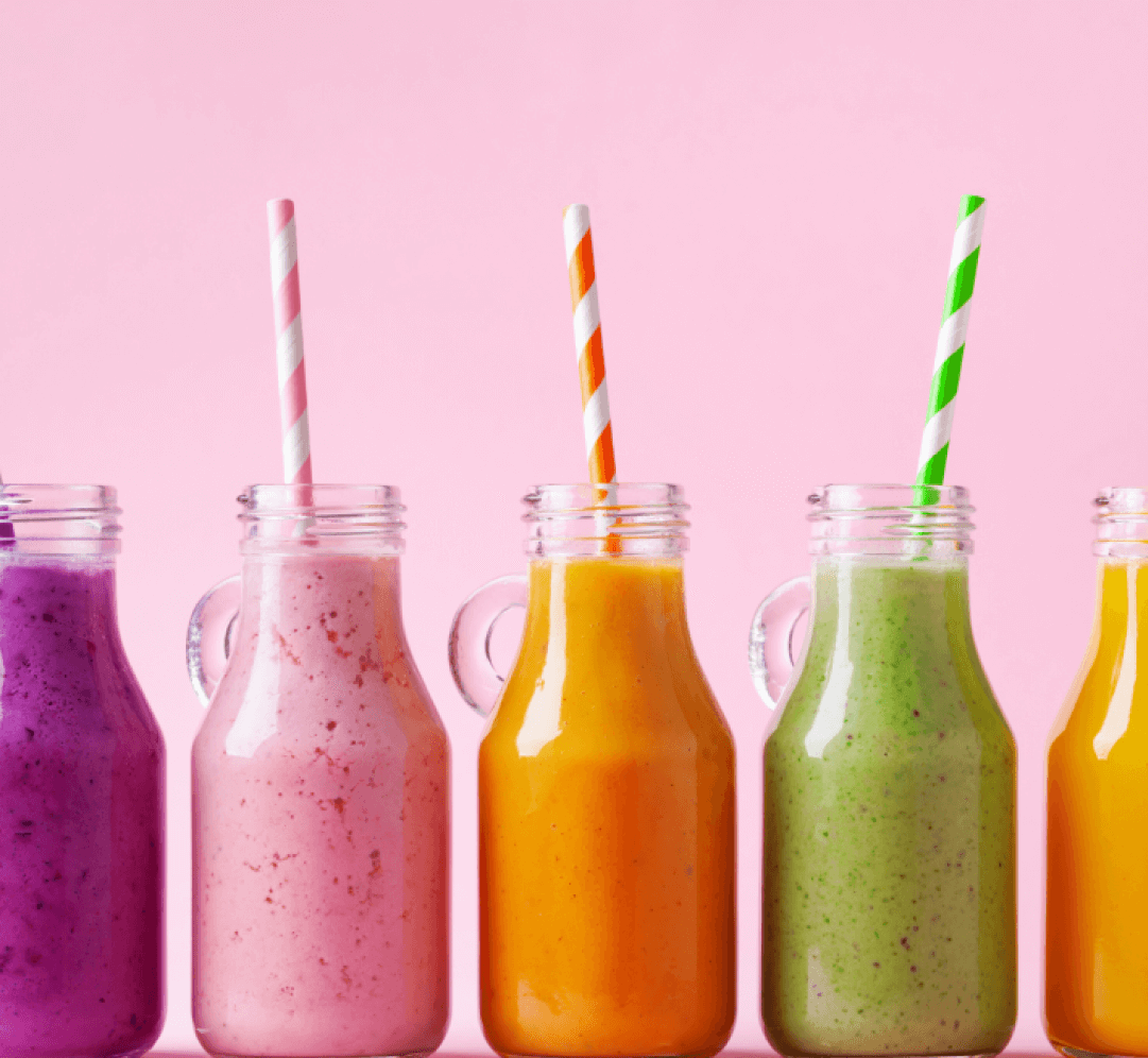 Line of bright juice jars with straws on a pink background