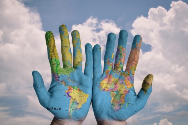 Puffy clouds in a blue sky with hands in front on which is painted a map of the world